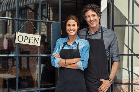 Two cafe owners smiling next to open sign